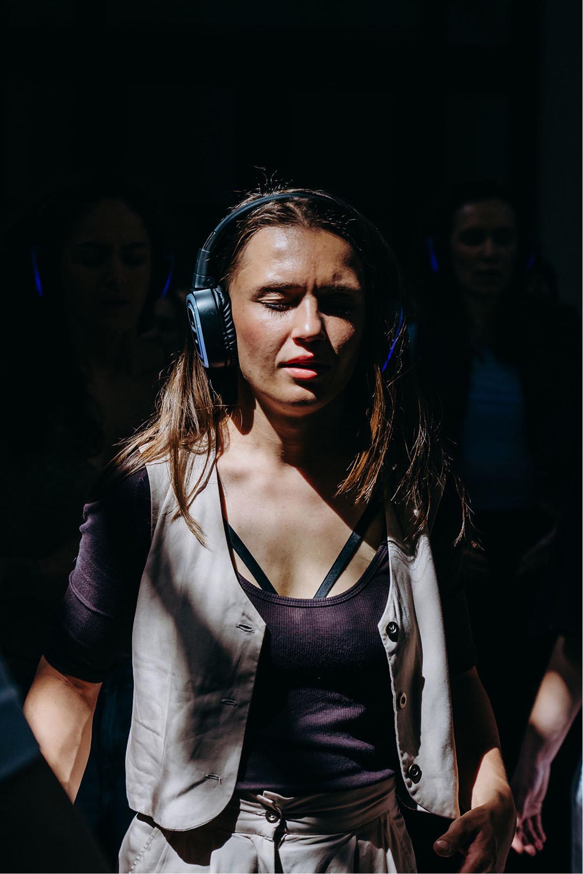 Žena se sluchátky a zavřenýma očima v pruhu světla